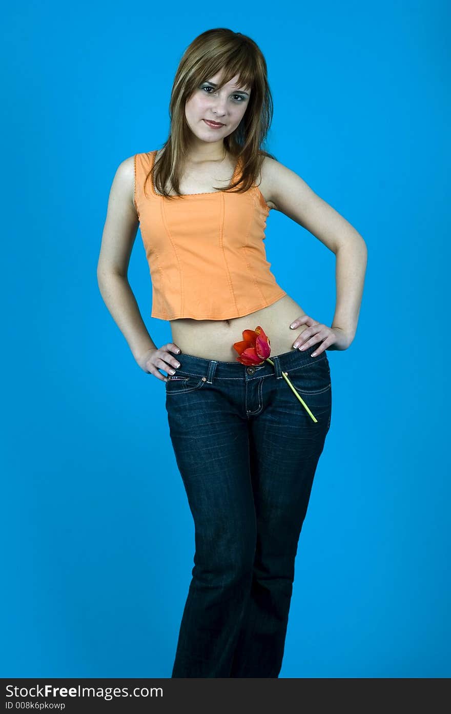 Beautiful young girl smiling and having a red tulip at her waist, like a pistol; isolated on blue background. Beautiful young girl smiling and having a red tulip at her waist, like a pistol; isolated on blue background