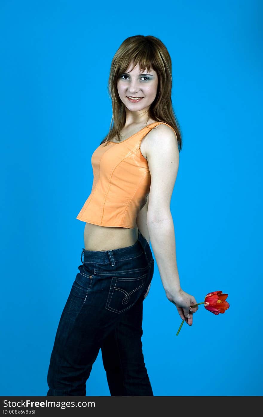 Young girl with nice looks and make-up, smiling and looking happy; holding a red tulip at her back; isolated on blue. Young girl with nice looks and make-up, smiling and looking happy; holding a red tulip at her back; isolated on blue