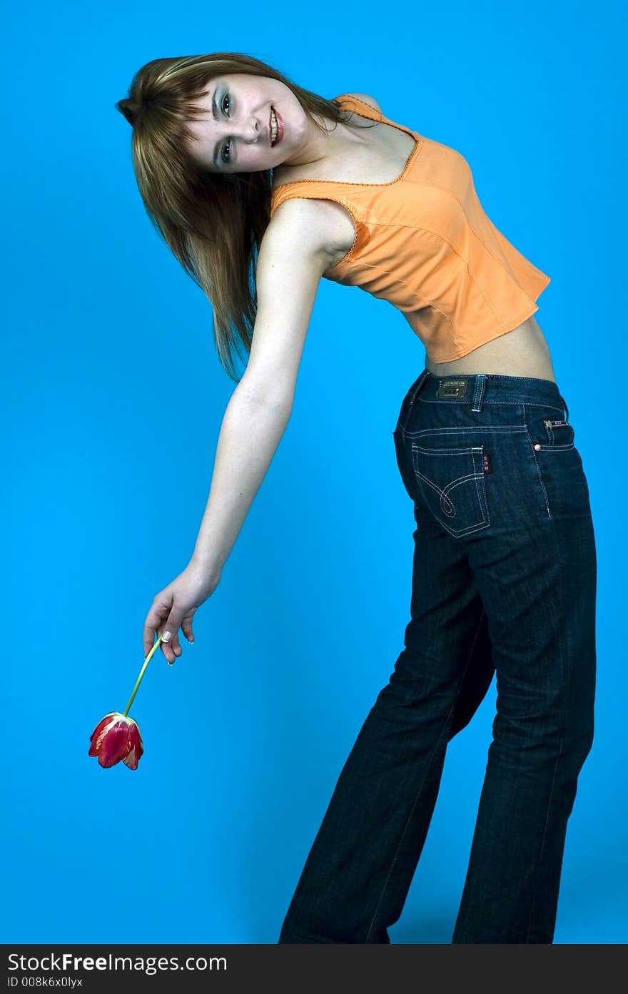 Beautiful young girl posing in a studio, holding a red tulip in her hand and stretching over her back, smiling, isolated on blue background. Beautiful young girl posing in a studio, holding a red tulip in her hand and stretching over her back, smiling, isolated on blue background