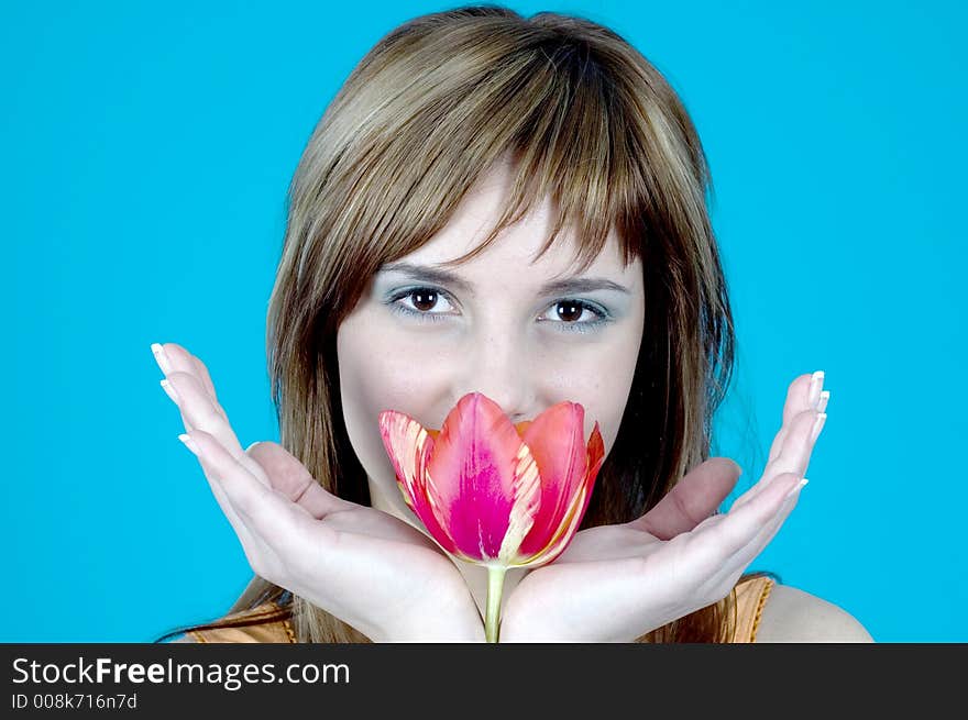 Portrait of a beautiful young girl smiling and holding a tulip between her hands, nice make-up; isolated on blue background. Portrait of a beautiful young girl smiling and holding a tulip between her hands, nice make-up; isolated on blue background