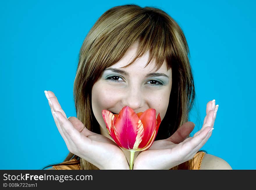 Portrait of a beautiful young girl smiling and holding a tulip between her hands, nice make-up; isolated on blue background. Portrait of a beautiful young girl smiling and holding a tulip between her hands, nice make-up; isolated on blue background