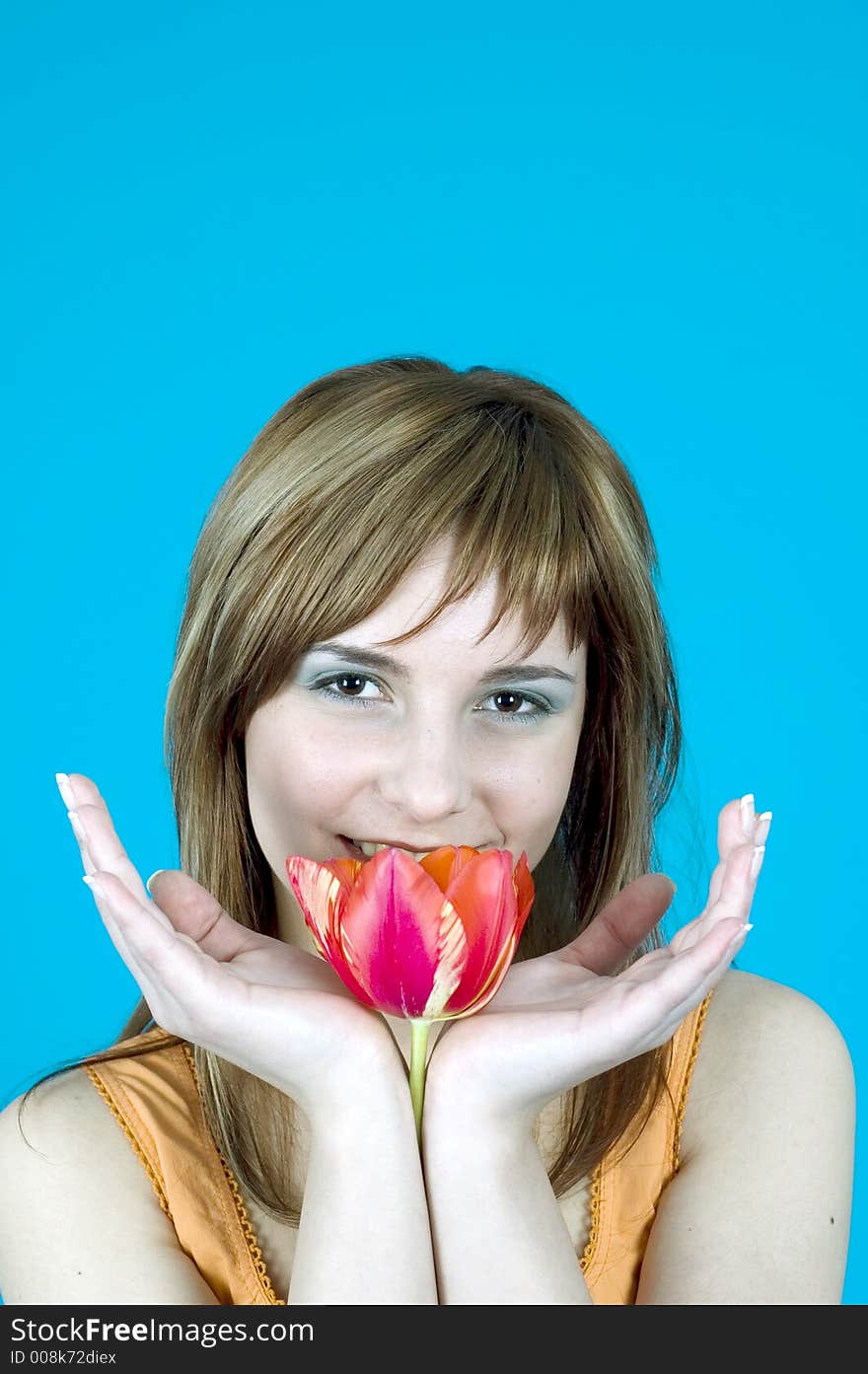 Portrait of a beautiful young girl smiling and holding a tulip between her hands, nice  make-up; isolated on blue background. Portrait of a beautiful young girl smiling and holding a tulip between her hands, nice  make-up; isolated on blue background