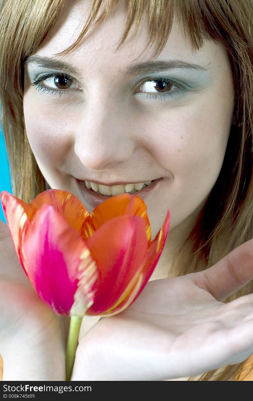 Portrait of a beautiful young girl smiling and holding a tulip between her hands, nice  make-up; isolated on blue background. Portrait of a beautiful young girl smiling and holding a tulip between her hands, nice  make-up; isolated on blue background