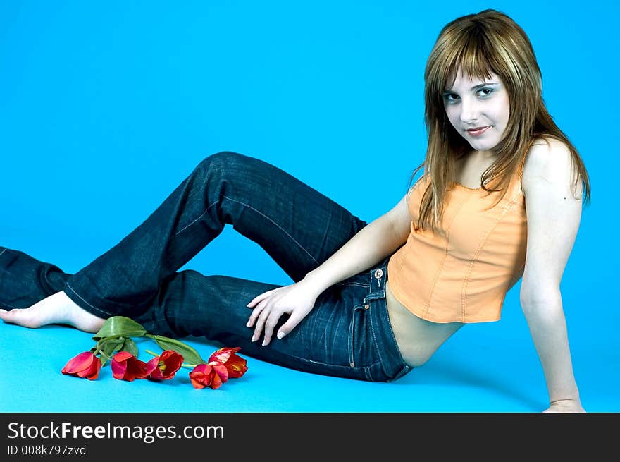 Portrait of a beautiful young girl laying on the floor next to a bouquet of tulips; nice smile; teenager looks and attitude; isolated on blue background. Portrait of a beautiful young girl laying on the floor next to a bouquet of tulips; nice smile; teenager looks and attitude; isolated on blue background