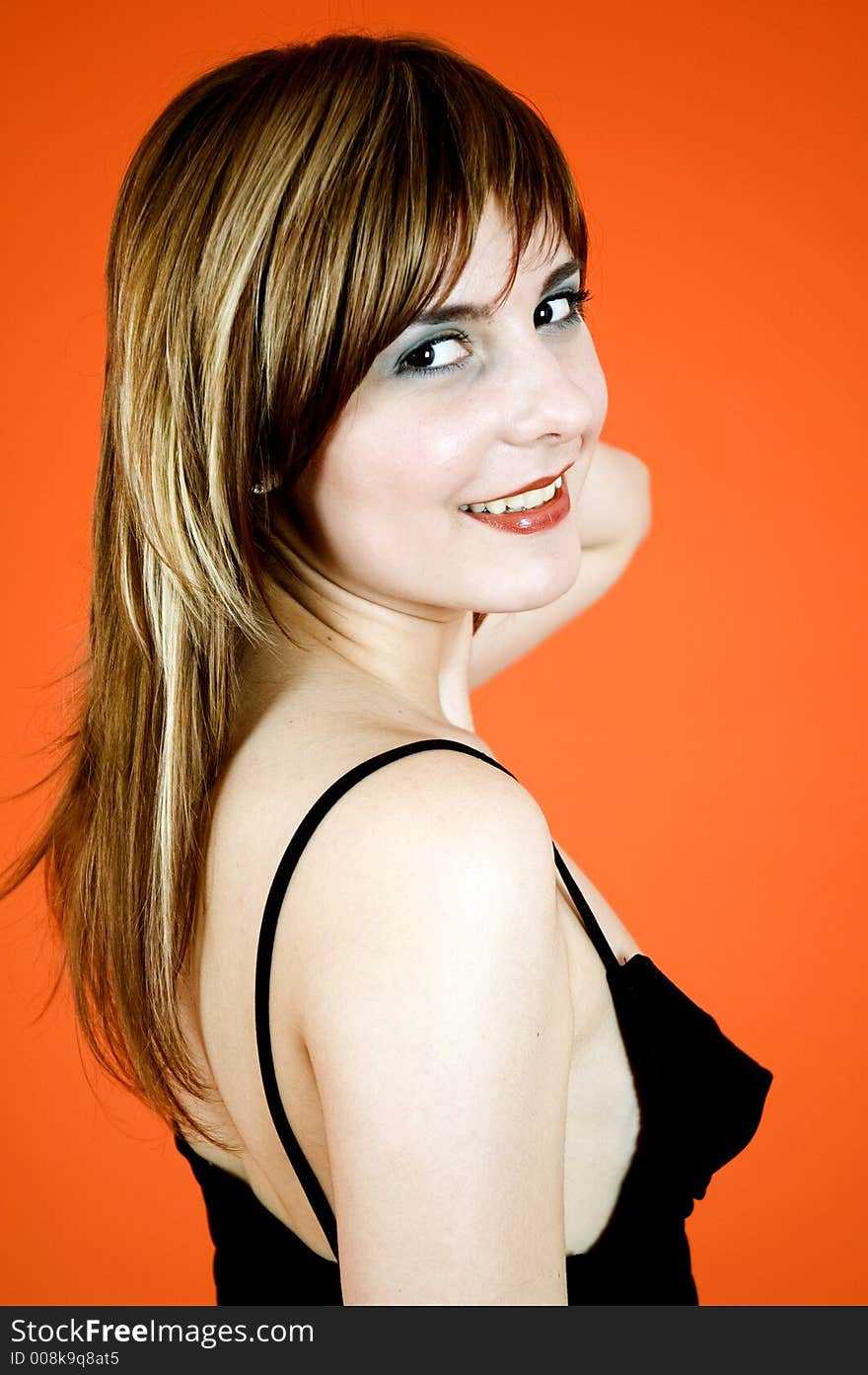 Beautiful young girl wearing a black dress posing in a studio, smiling and looking happy; isolated on orange background. Beautiful young girl wearing a black dress posing in a studio, smiling and looking happy; isolated on orange background.