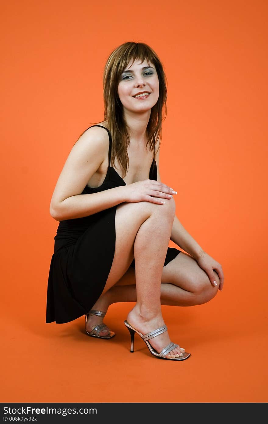 Portrait of a young girl with nice looks and make-up wearing a black casual dress posing in a studio, isolated on orange background. Portrait of a young girl with nice looks and make-up wearing a black casual dress posing in a studio, isolated on orange background