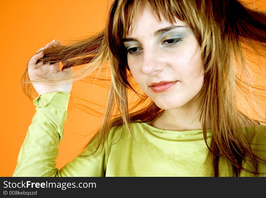 Beautiful young girl posing in a studio, pulling her hair with both hands, looking like she's thinking about the next haircut or colour; isolated on orange. Beautiful young girl posing in a studio, pulling her hair with both hands, looking like she's thinking about the next haircut or colour; isolated on orange