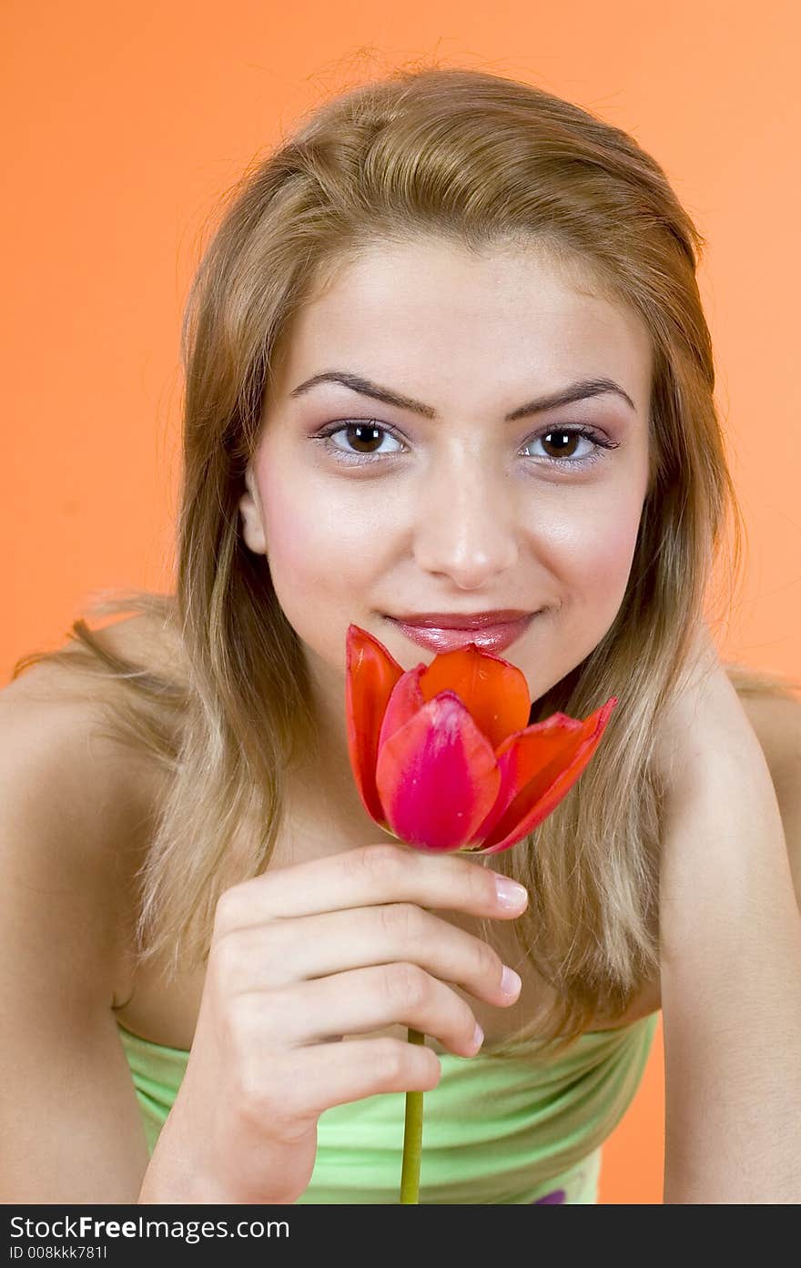 Beautiful blond girl smelling a red tulip and looking relaxed; orange background. Beautiful blond girl smelling a red tulip and looking relaxed; orange background