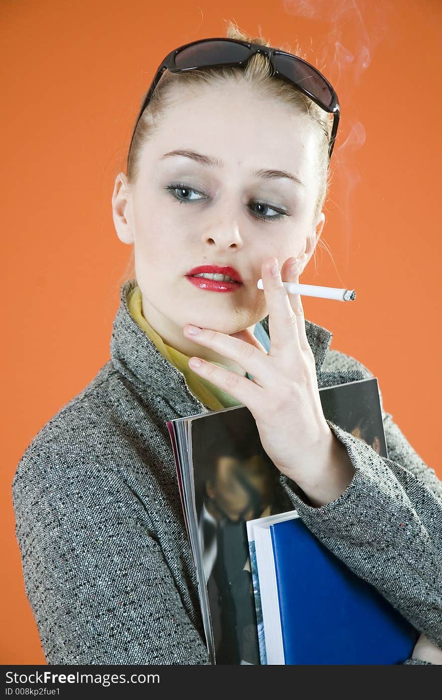 Portrait of a beautiful young blond with glamour look and make-up holding some books and smiking a cigar; isolated on orange. Portrait of a beautiful young blond with glamour look and make-up holding some books and smiking a cigar; isolated on orange