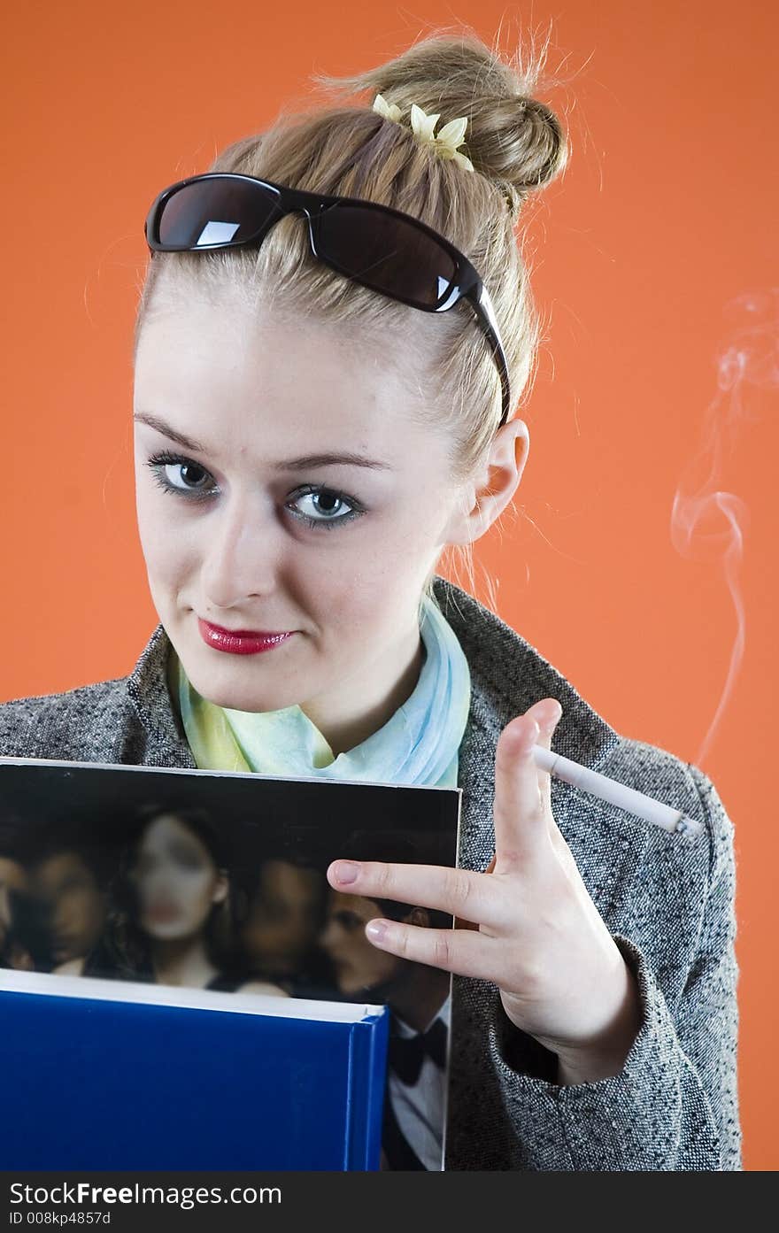 Portrait of a beautiful young blond with glamour look and make-up holding some books and smiking a cigar; isolated on orange. Portrait of a beautiful young blond with glamour look and make-up holding some books and smiking a cigar; isolated on orange