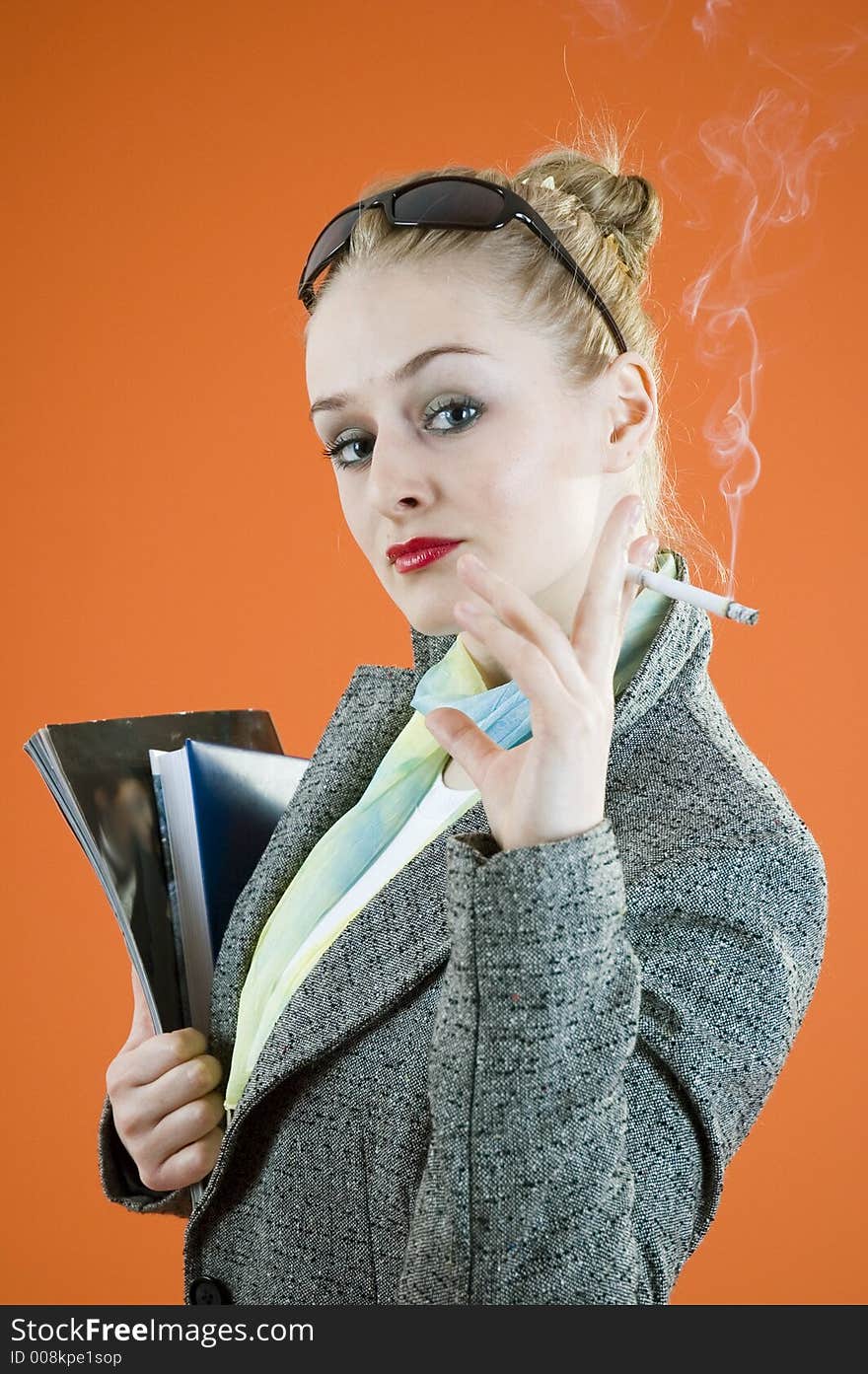 Portrait of a beautiful young blond with glamour look and make-up holding some books and smiking a cigar; isolated on orange. Portrait of a beautiful young blond with glamour look and make-up holding some books and smiking a cigar; isolated on orange