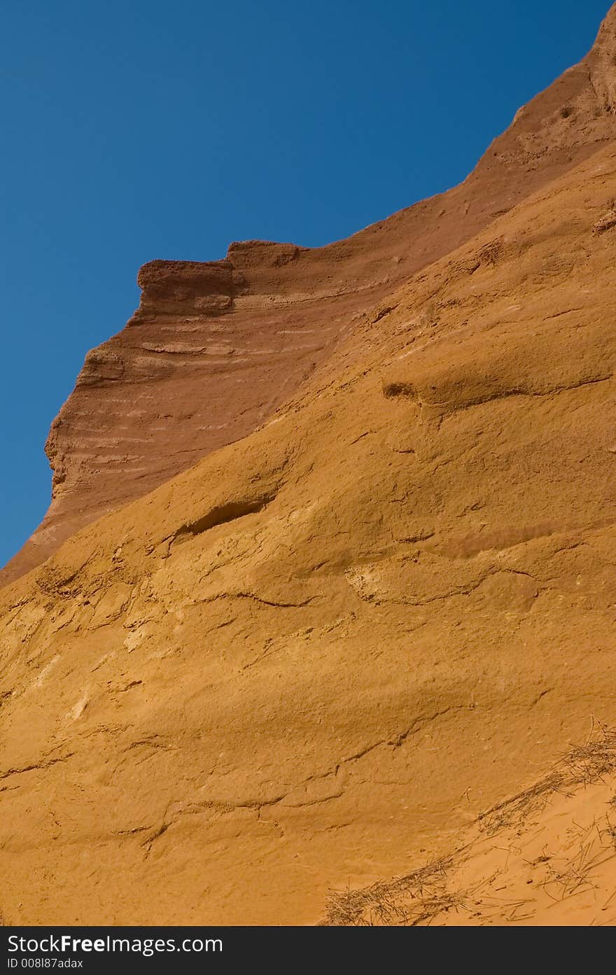 Close crop of ochre sands at Rousillon, France, with bright red and yellow ochre against bold blue sky. Close crop of ochre sands at Rousillon, France, with bright red and yellow ochre against bold blue sky