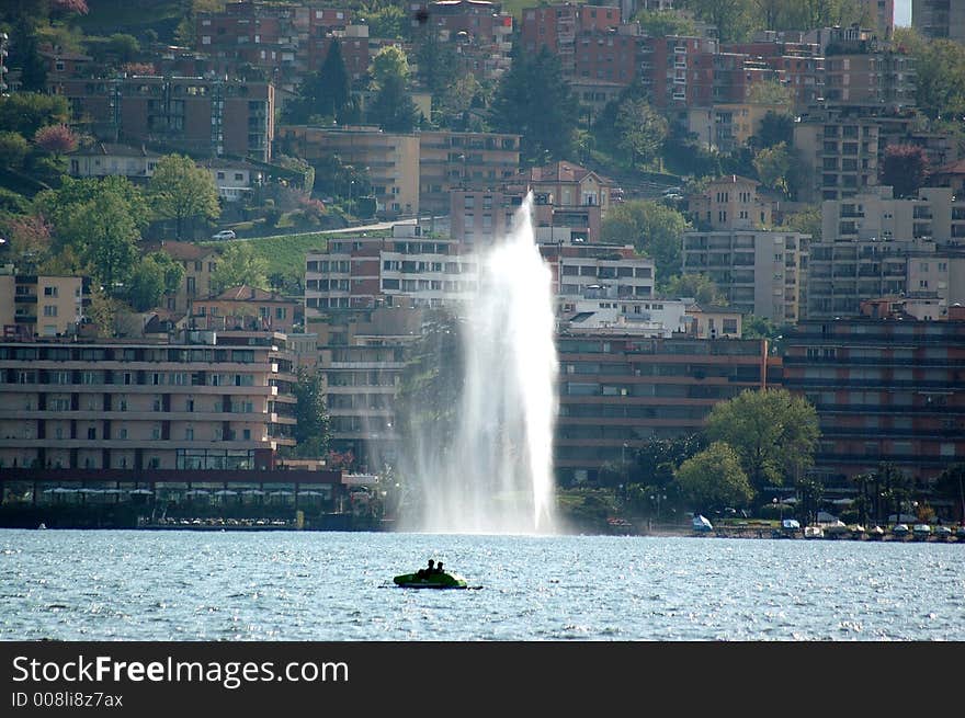 Lake of lugano in a sunny day with a boat and a fountain. on the background Lugano Paradiso. Lake of lugano in a sunny day with a boat and a fountain. on the background Lugano Paradiso