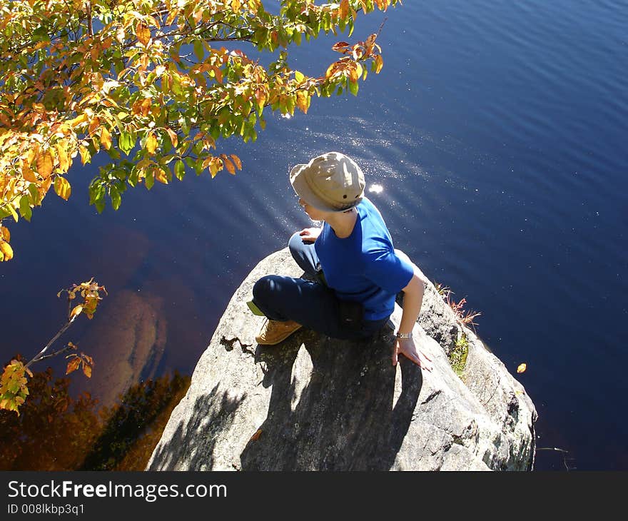 Girl sits ashore on large stone