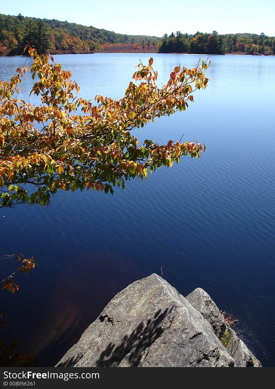 Triangle shape stone ashore. Small lake in foliage time