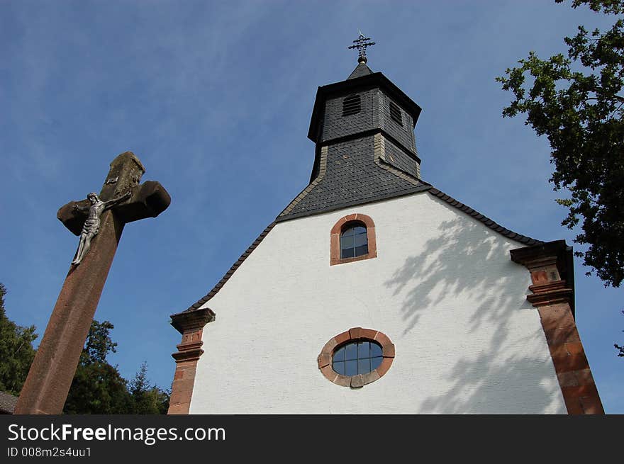 A view of an old German Catholic church and a crucifix cross in Hohenecken, Germany. A view of an old German Catholic church and a crucifix cross in Hohenecken, Germany