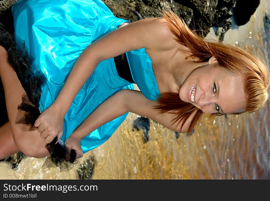 A pretty teen sitting on the rocks at the beach in a formal dress. A pretty teen sitting on the rocks at the beach in a formal dress.