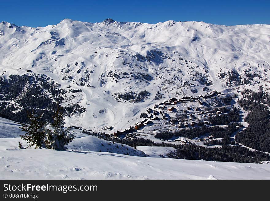 A panoramic view on a chain of alpine snow peaks with a small ski resort village. A panoramic view on a chain of alpine snow peaks with a small ski resort village