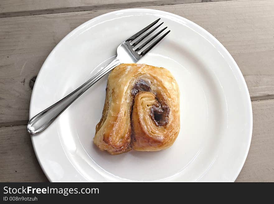 Warm cinnamon roll on white plate with fork