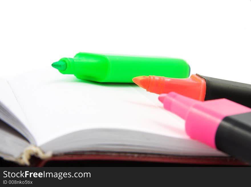 Three colourful markers on white diary. Three colourful markers on white diary.