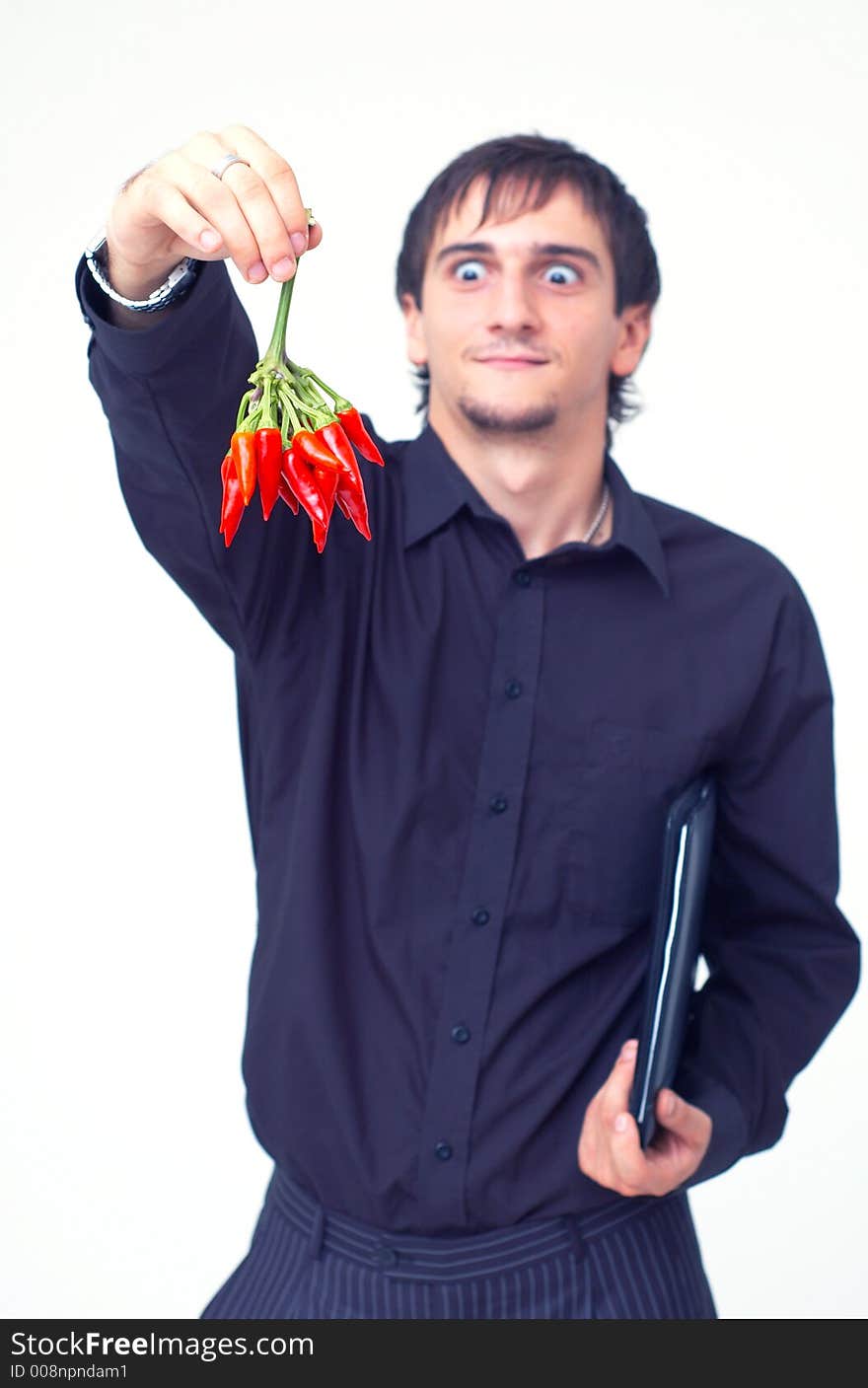 Young boy with black shirt holding a buch of red chilli peppers and having a funny expression; white background. Young boy with black shirt holding a buch of red chilli peppers and having a funny expression; white background