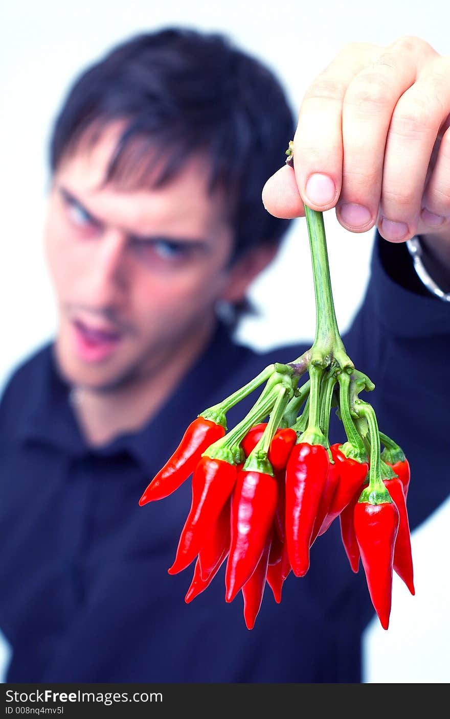 Young boy with black shirt holding a buch of red chilli peppers and having a funny expression; white background. Young boy with black shirt holding a buch of red chilli peppers and having a funny expression; white background