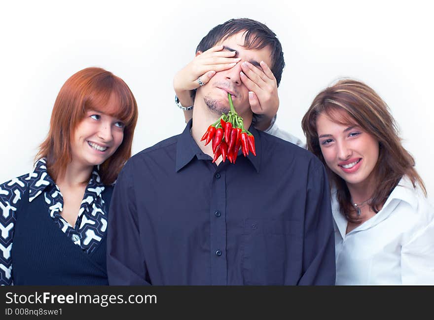 Guy holding a bunch of red chilli peppers in his mouth and two beautiful girls covering his eyes with the hands. Guy holding a bunch of red chilli peppers in his mouth and two beautiful girls covering his eyes with the hands