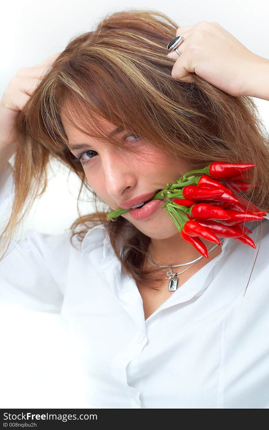 Portrait of a beautiful young girl holding a bunch of red chilli peppers in her mouth and pulling on her hair. Portrait of a beautiful young girl holding a bunch of red chilli peppers in her mouth and pulling on her hair