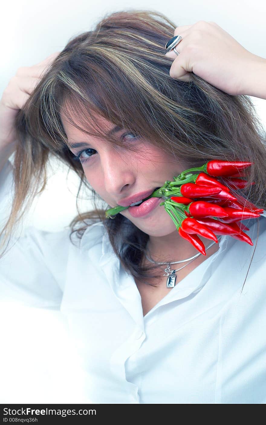 Portrait of a beautiful young girl holding a bunch of chilli peppers in her mouth and pulling on her hair. Portrait of a beautiful young girl holding a bunch of chilli peppers in her mouth and pulling on her hair