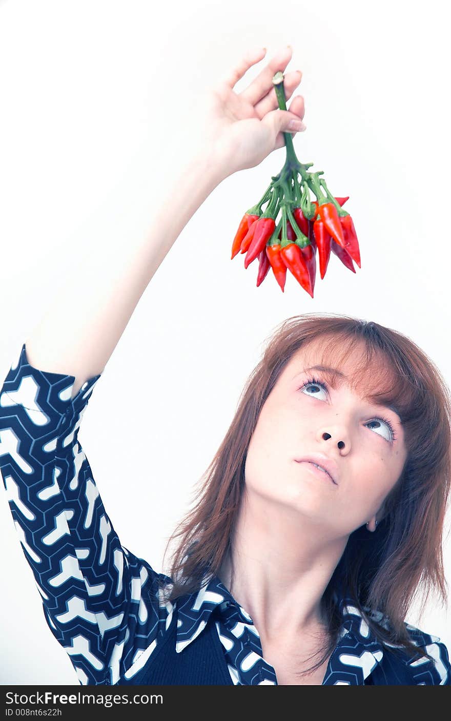 Portrait of a beautiful young girl holding a bunch of red chilli peppers over her head and looking at them; white background. Portrait of a beautiful young girl holding a bunch of red chilli peppers over her head and looking at them; white background