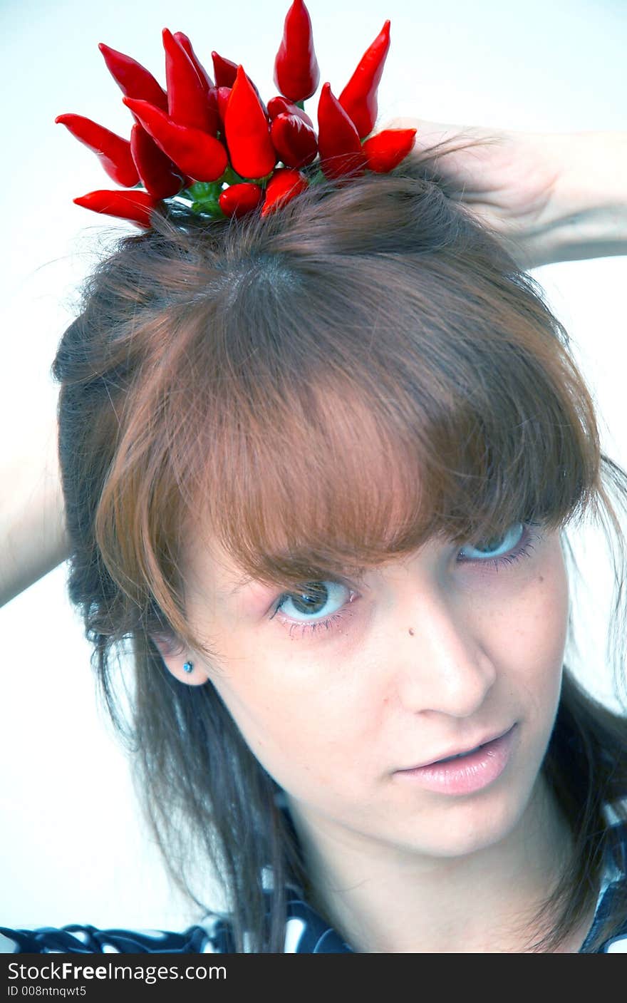 Portrait of a beautiful young girl holding a bunch of red chilli peppers over her head and looking at them; white background. Portrait of a beautiful young girl holding a bunch of red chilli peppers over her head and looking at them; white background