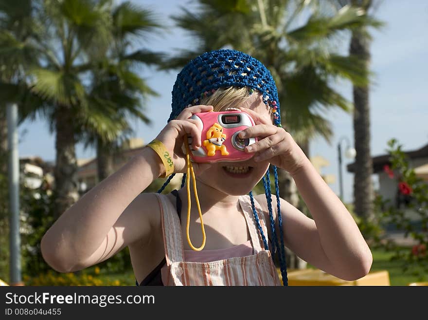 A 7 years old playing with a toy camera with palm trees as background and sunny sky. A 7 years old playing with a toy camera with palm trees as background and sunny sky