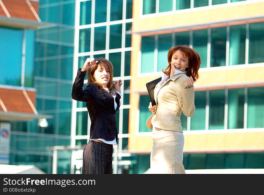 Two beautiful business women jumping in front of a business building, being happy for their success. Two beautiful business women jumping in front of a business building, being happy for their success