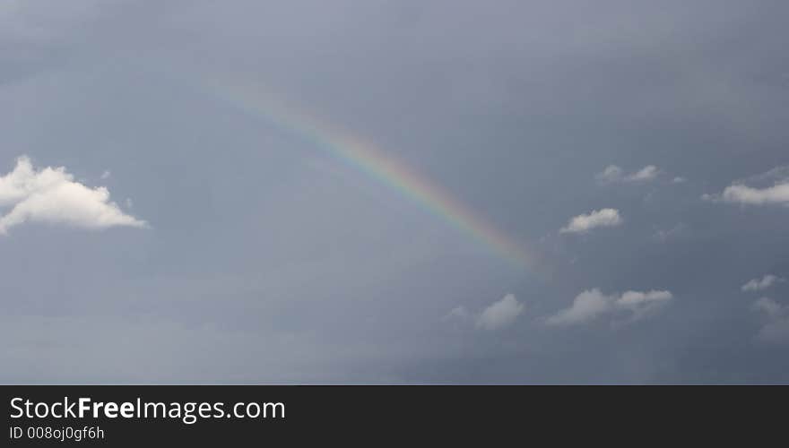 A rainbow in dark winter sky with white clouds. A rainbow in dark winter sky with white clouds