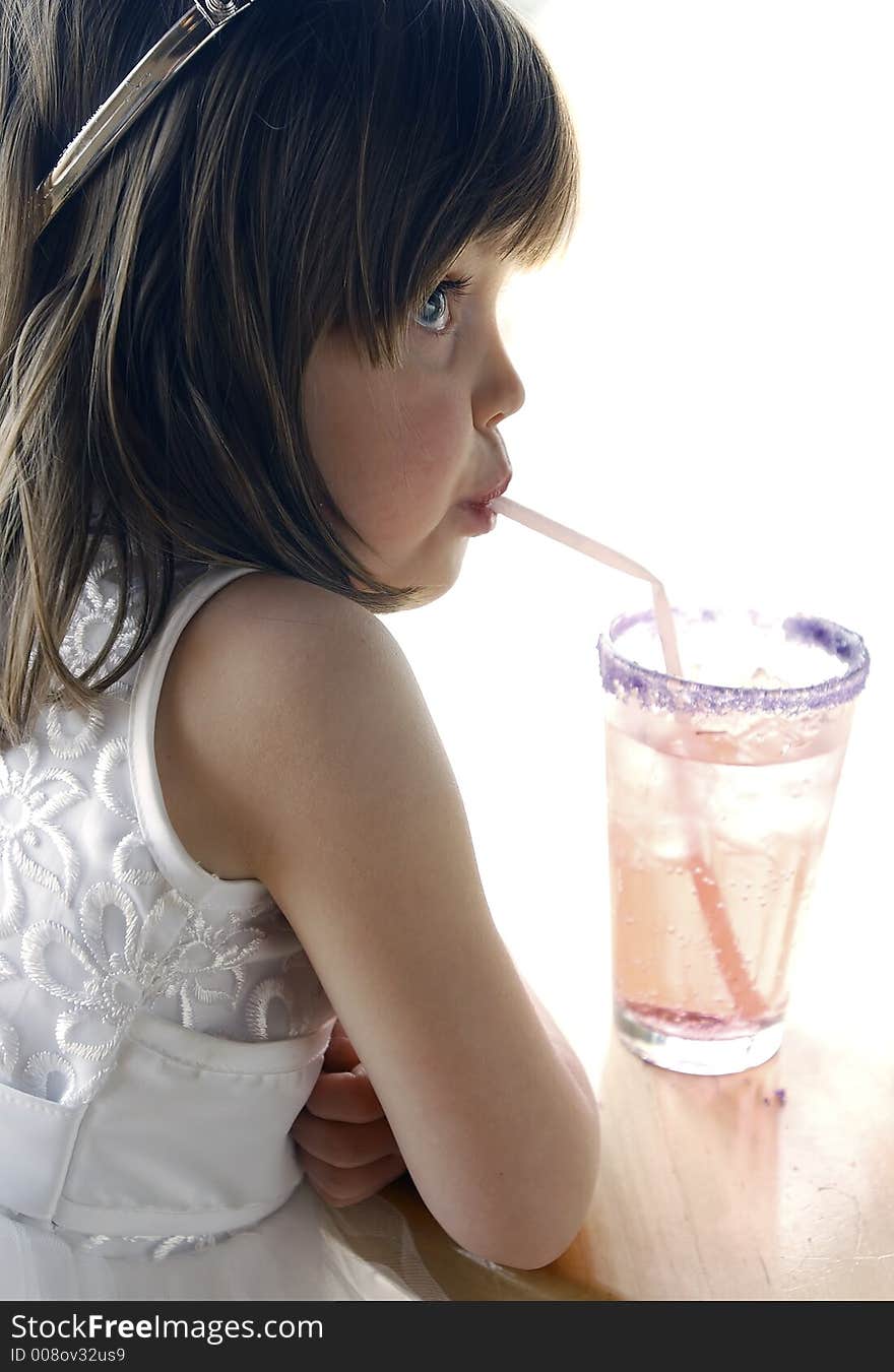 Young girl sitting at a table drinking a soda with a straw. Girl is wearing a princess costume and crown. Looking away from the camera. Young girl sitting at a table drinking a soda with a straw. Girl is wearing a princess costume and crown. Looking away from the camera.