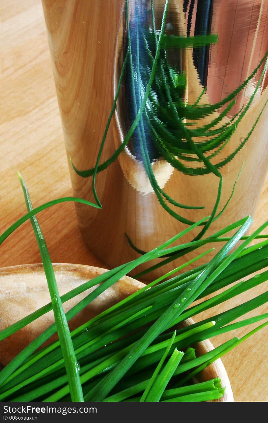 Chive leaves in a wooden bowl reflected in metal mug. Chive leaves in a wooden bowl reflected in metal mug