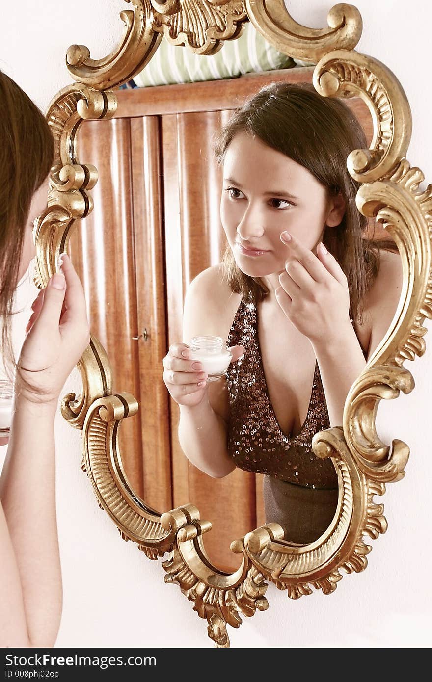 Auburn-haired girl, young woman putting cream in front of a mirror