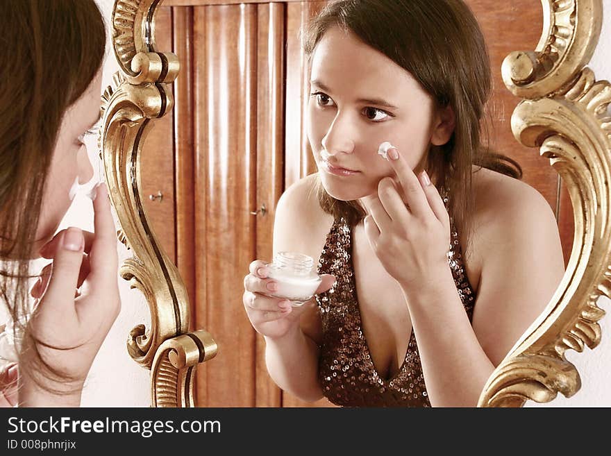 Auburn-haired girl, young woman putting cream in front of  a mirror