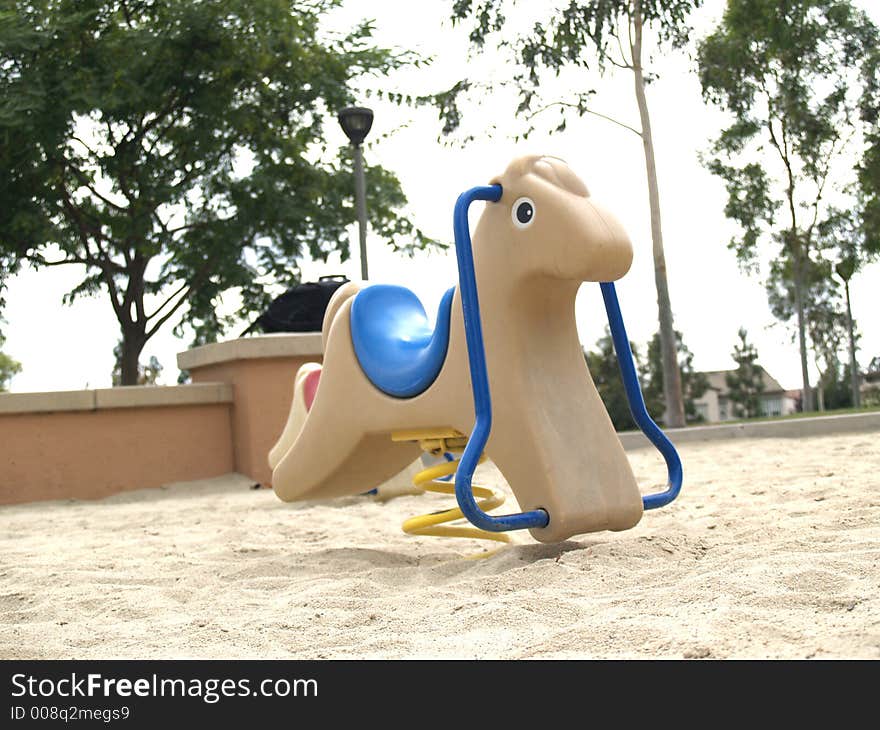 Beige kiddy horse with blue seat in a sand playground. Beige kiddy horse with blue seat in a sand playground