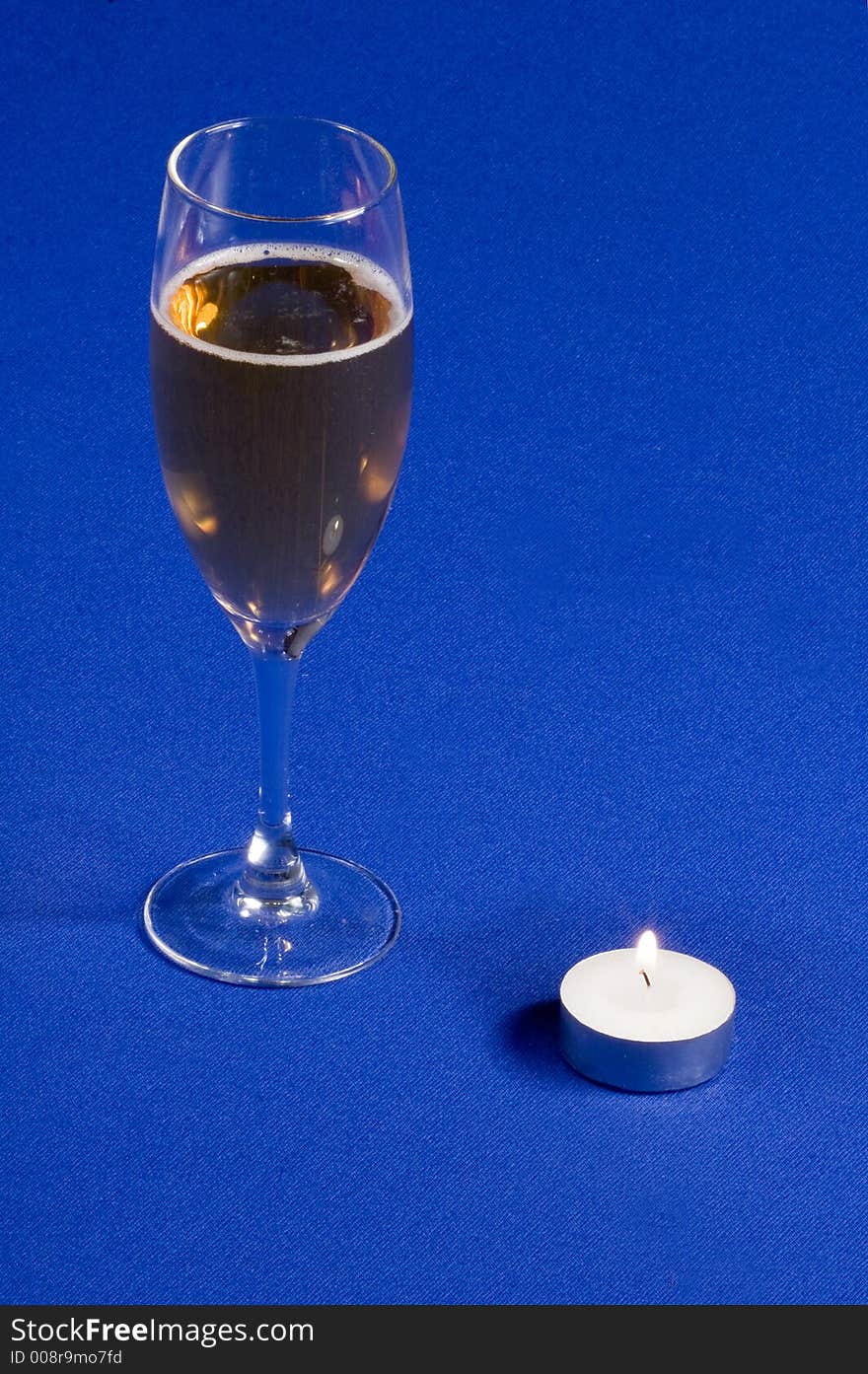 A glass of champagne with candle on blue background