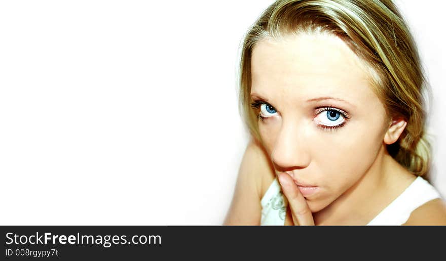 A young blond woman with blue eyes in front of white background is holding her finger in front of her mouth. A young blond woman with blue eyes in front of white background is holding her finger in front of her mouth