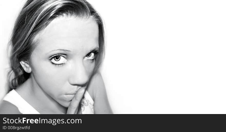 A young blond woman with blue eyes in front of white background is holding her finger in front of her mouth. A young blond woman with blue eyes in front of white background is holding her finger in front of her mouth