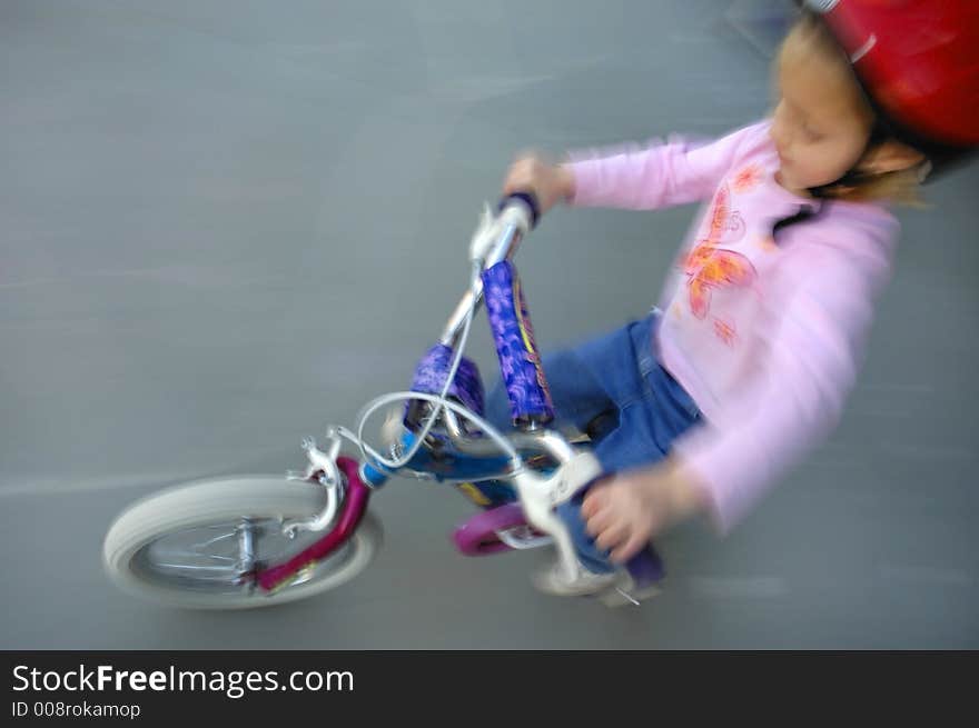 Motion shot of little girl biking with red helmet