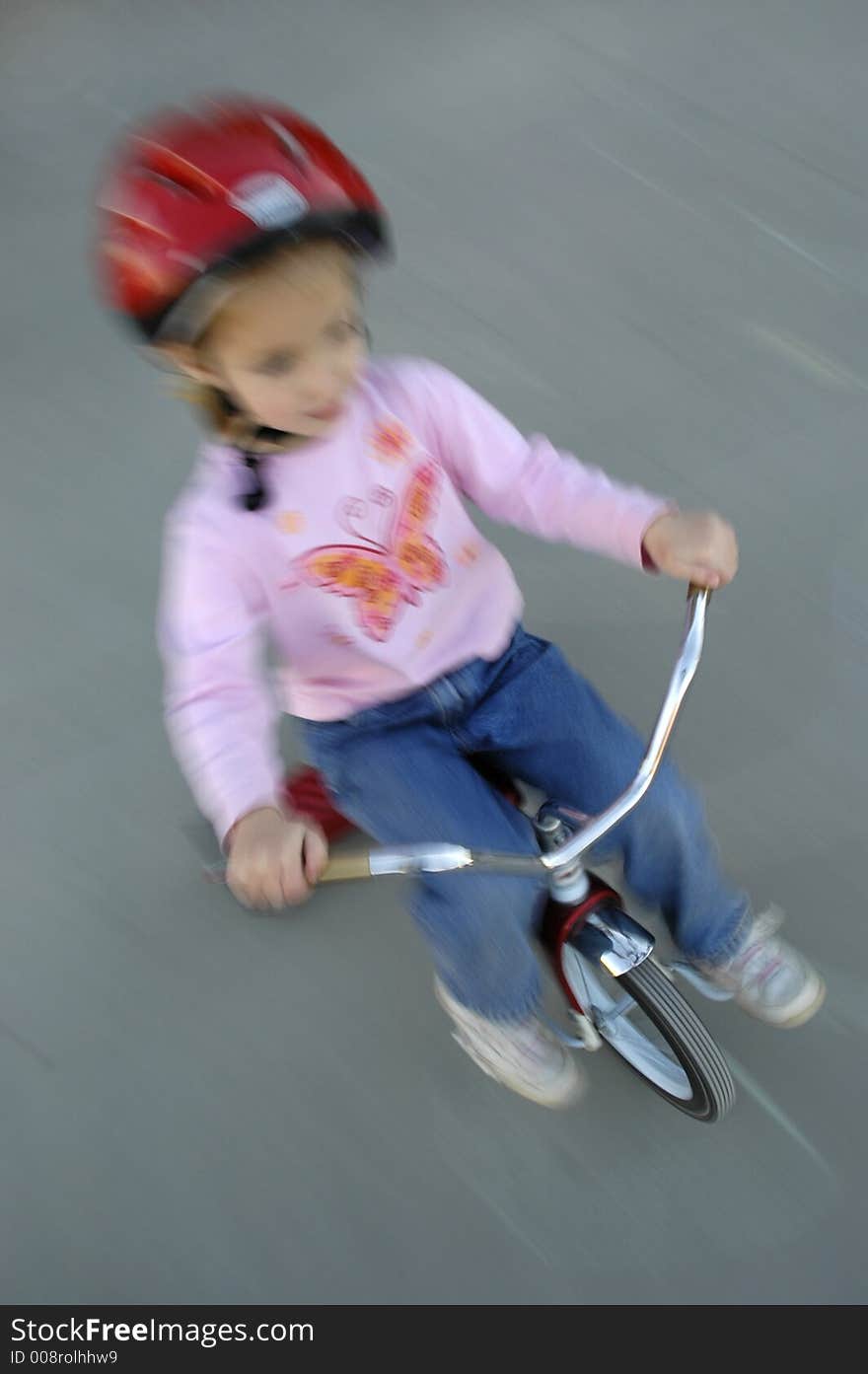 Motion shot of little girl biking with red helmet