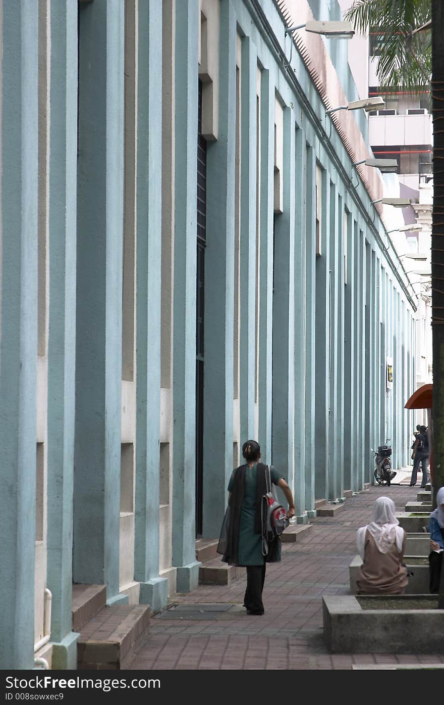 People along a blue building facade with vertical pillars. People along a blue building facade with vertical pillars