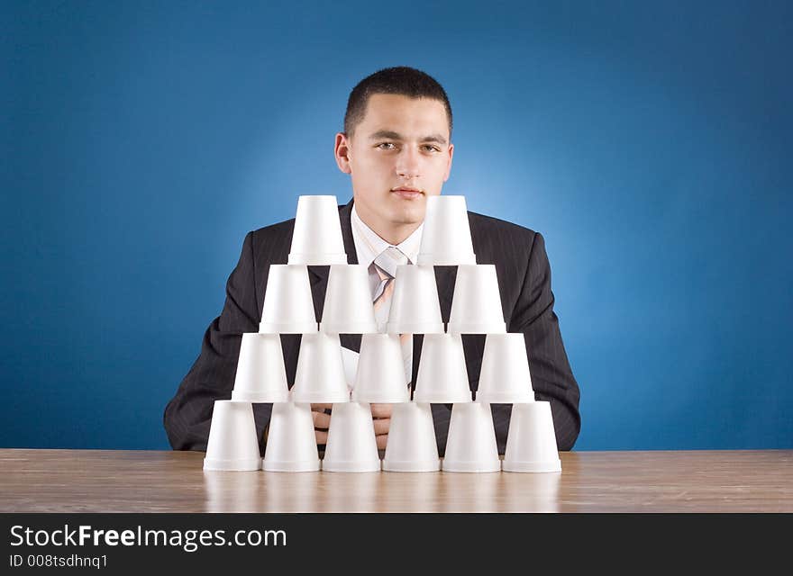 Businessman building cups' pyramid (blue background)