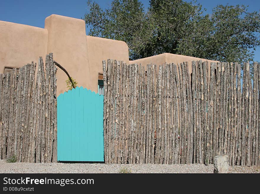 Turquoise gate with wooden pole fence and stucco building in the background. Turquoise gate with wooden pole fence and stucco building in the background