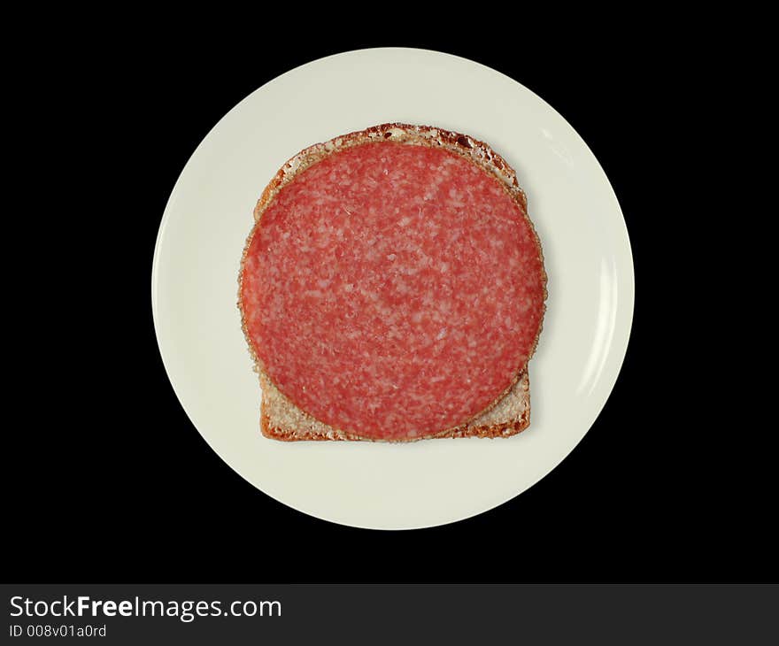 A slice of bread with salami on a white plate, isolated on black. A slice of bread with salami on a white plate, isolated on black.