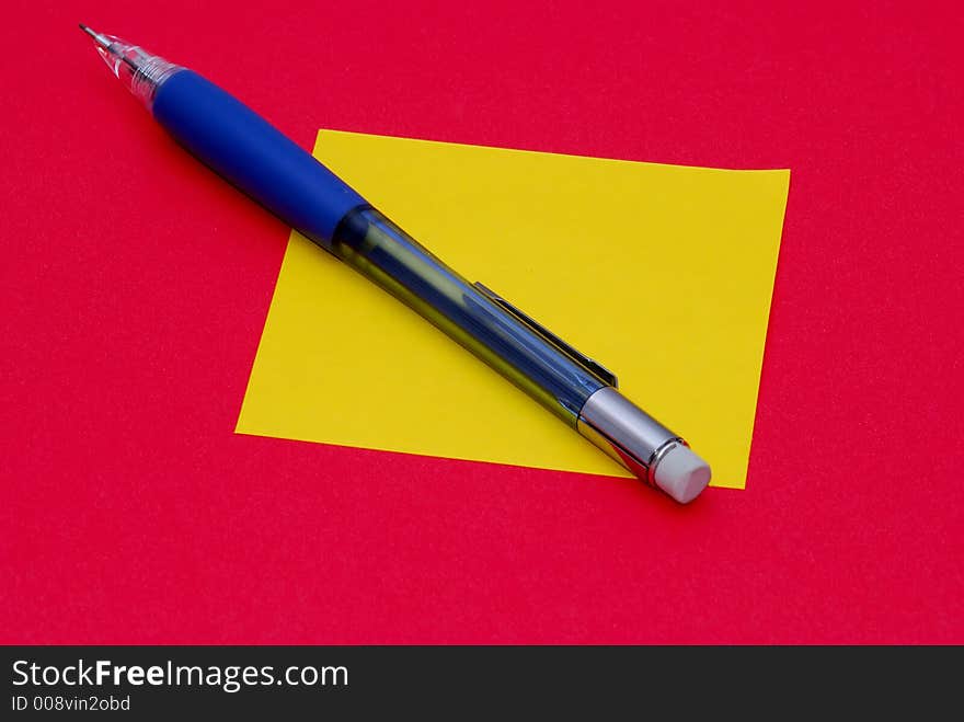 A pencil and a sticky note on a red background. A pencil and a sticky note on a red background