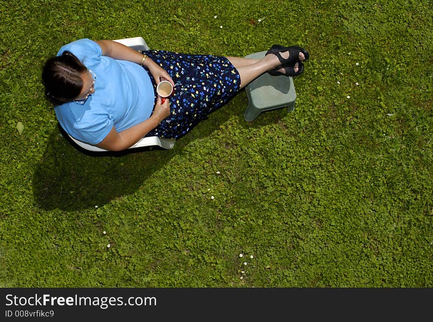 After a hard day's work, a woman puts her feet up, with a cup of tea in the garden. Space for text on the green of the grass. After a hard day's work, a woman puts her feet up, with a cup of tea in the garden. Space for text on the green of the grass.